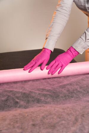 Beautician spreads a sheet on a massage couch on a light backgroundの写真素材
