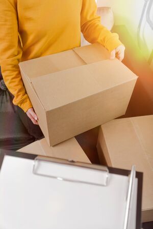close-up young woman on a sunny day sends delivery of things in a box. gives a cardboard box to the courier, vertical photoの写真素材