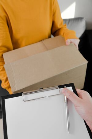 Close-up young woman sends delivery of things in a box. Passes a cardboard box to the courier, vertical photoの写真素材