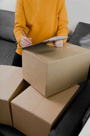 Close-up of a young girl puts a signature on the form of delivery of things. Things are packed in cardboard. Customer received package. vertical photoの写真素材