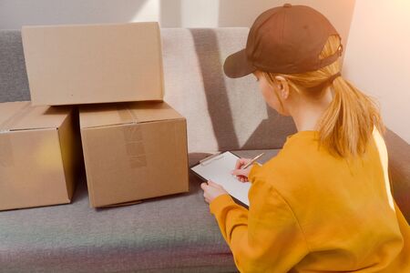 girl signs documents to send closed cardboard boxes. The courier carries unnecessary things at homeの写真素材