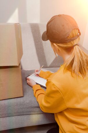 a girl on a sunny day in a black cap signs documents for sending boxes on a sunny dayの写真素材