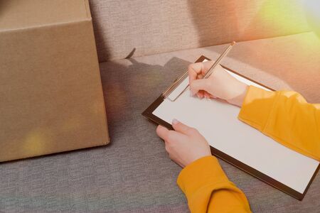 girl manager makes a list of things that lie in cardboard boxes. Inventory of the warehouse. close-up order formの写真素材