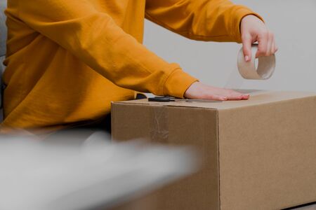 female hands paste a cardboard box closeup on a light background with adhesive tape. Pack the goods for shipmentの写真素材