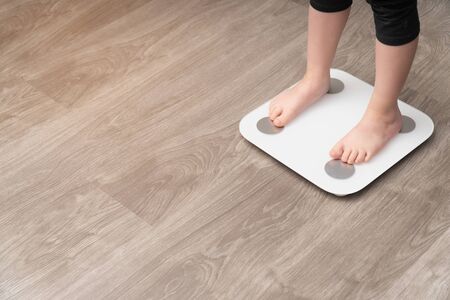 vertical photo closeup of baby's legs on a measuring scale. Childhood obesity control concept, side...