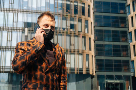 Portrait of a business man in a mask who is talking on a smartphone. Concept of businessman against...
