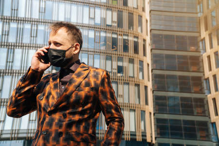 Portrait of a business man in a mask who is talking on a smartphone. Concept of businessman against virus and pandemic.の写真素材