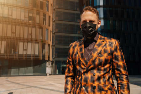 Portrait of a young man in medical black mask looking away forward against the background of business center. average plan.の写真素材