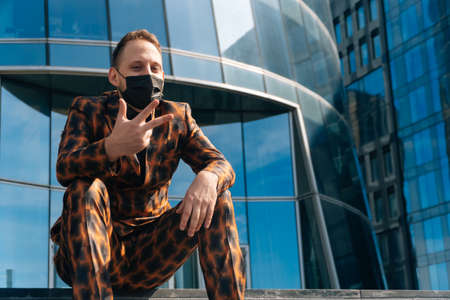 Portrait of a cheerful European man in a medical mask on the background of a business center. middle plan businessman indulges on the steps in a business suit.の写真素材