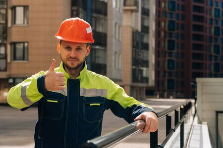 a clean builder shows sincere emotions of joy. man in special clothes and a hard hat, against the background of a ready made business centerの写真素材