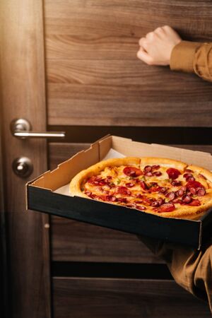 A vertical frame of the girl holds a pizza and knocks on the door. the concept of food delivery.の写真素材