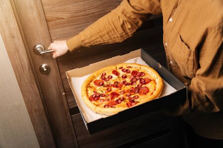 Closeup women hands hold a box of new pizza. The girl opens the door and holds pepperoni.の写真素材