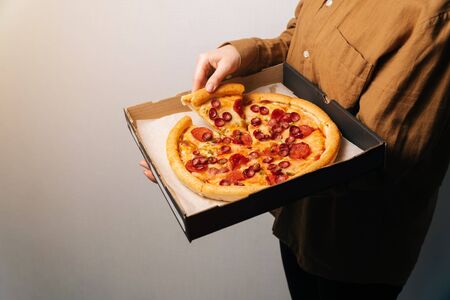 The female hand takes the first new piece of pepperoni pizza out of the delivery box.on a light background space.の写真素材