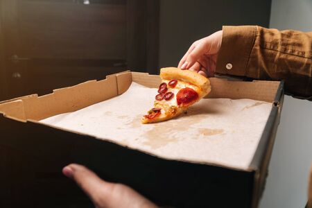 Girl picks up last piece of pepperoni pizza from box closeup.の写真素材