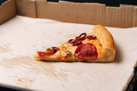 Closeup of the last whole slice of pepperoni pizza in a cardboard paper box on dark background. fast food concept on the table.の写真素材