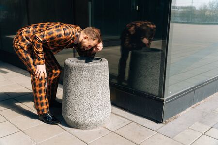 A young male manager vomits in the trash can from eating. The concept of food poisoning in the...