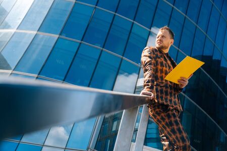 A young businessman stands on a blue background in a business suit holding documents. The concept of meeting businessmen.の写真素材