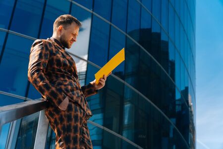 A young businessman stands on a blue background in a business suit holding documents. The concept of meeting businessmen.の写真素材