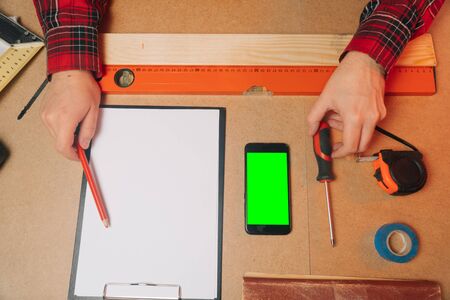 In the workshop, a man measures the wooden part on a smartphone. The concept of using a mobile app for a construction companyの写真素材
