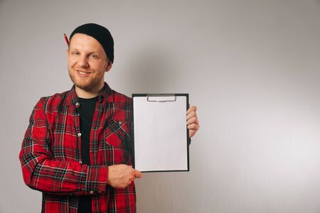 A portrait of a male builder on a white background of insulation that holds paper and a folder in...