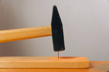 Close-up shot of a hammer hammering a nail on a light background. The concept of carpentry on the table.の写真素材