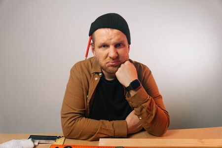 Portrait of a male builder with a beard in uniform who is in doubt. Woodworking workshop in a factory. home construction conceptの写真素材