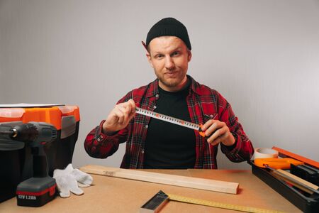 The carpenter is holding a centimeter of tape. A roulette Caucasian rutal man measures a wooden board. guy a carpenter with a beard works in a carpentry workshopの写真素材