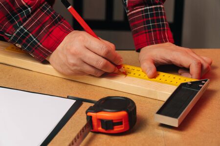 A young Caucasian guy a carpenter with a beard works in a carpentry workshop. Builder measures a wooden board.の写真素材