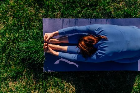 A young girl is training outdoors. The athlete performs the crease exercise to extend the back. Lying on a grass matの写真素材