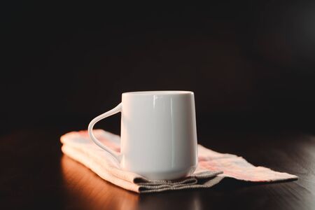 A white beautiful cup of tea or freshly brewed coffee is standing on a beautiful rag against a dark background. scattered roasted grainsの写真素材