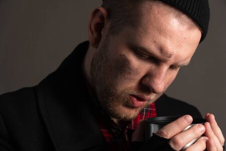 portrait of a unhappy unemployed man who drinks from a tin mug. The concept of survival of the poor on the street.の写真素材