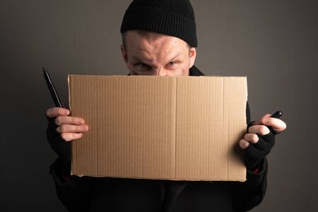 portrait a young man who holds a felttip pen in his mouth to write text on cardboard. begging concept.の写真素材