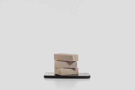 Cardboard brown paper boxes lie on a smartphone. The concept of selling goods through an online...