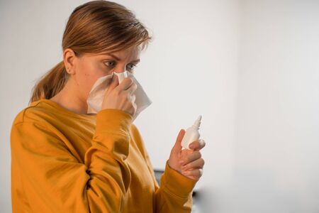 A young caucasian girl sneezes and covers her nose with a scarf. Viral infection snot. Hold a spray...