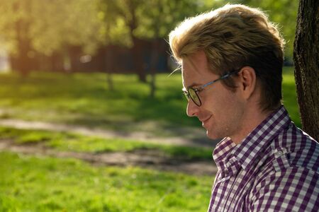 Portrait of a young handsome fair-haired man on a sunny day on a green background with summer grass....