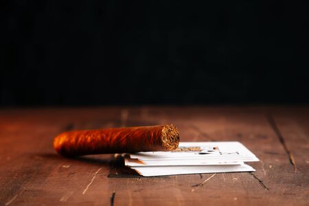 A cigar on the table next to a deck of cards on a dark brown table. The concept of smoking while playing poker.の写真素材