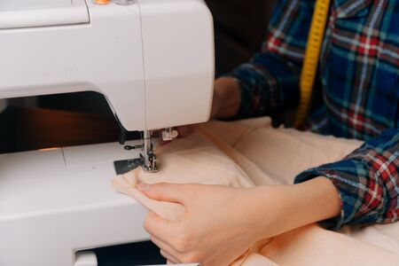 The seamstress inserts the cloth under the sewing machine for the overlock. A closeup view of...