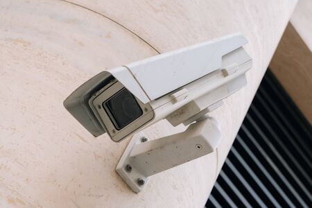 The ccTV camera is closeup against the background of the light business center. Protecting the surrounding area of the office buildingの写真素材