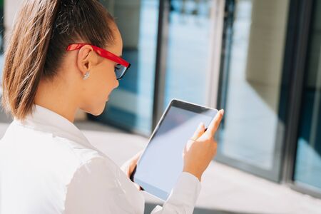 A girl businessman wearing glasses looks at the screen of her electronic tablet, the kind of shady woman who reads a letter online.の写真素材