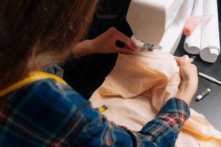 A seamstress inserts fabric under an overlock sewing machine. Top view of female hands holding a cotton fabric for sewing.の写真素材