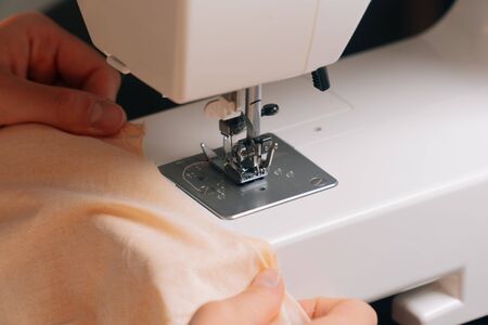 The seamstress inserts the cloth under the sewing machine for the overlock. A closeup view of...