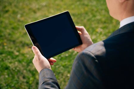 close up to hold the tablet in the hands of a man against a background of green grass. The concept...