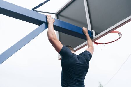 The fitness coach pulls up on the basketball basket crossbar. The concept of exercise on pectoral...