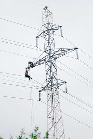 Male electricians make repairs on the electric tower. Power line against the sky.electrician work concept.June 6, 2020 Saint-Petersburg, Russiaのeditorial素材