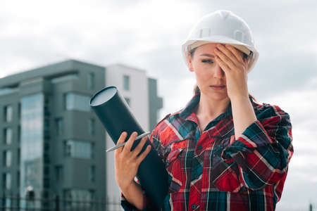 A brooding female builder with drawings of papers in her hands.