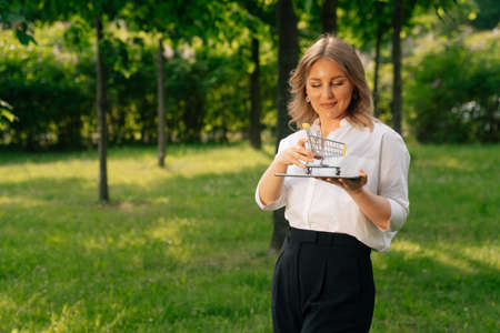 Stylish girl keeps a shopping cart and a digital tablet on the city premise.の写真素材