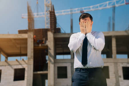 man covered his face with his hand in his palm, surprised apartment specialist, construction in progress concept, engineer in shockの写真素材