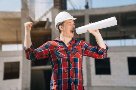 Portrait of a pensive man in a white helmet on a background of a building construction.の写真素材