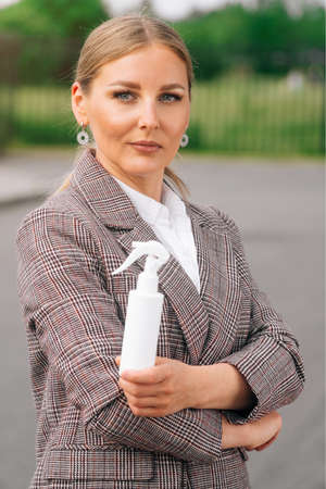 Stylish girl in an elegant suit holds bottle with an antiseptic. The concept of health care during a pandemicの写真素材