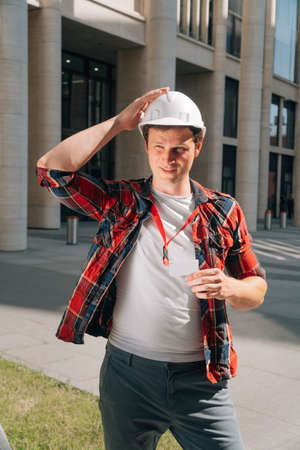 Portrait of a cheerful man in a white protective helmet with paper a background of a building constructionの写真素材